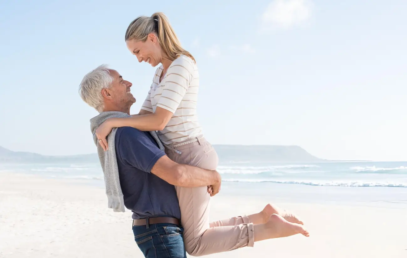 A senior man joyfully lifts a woman on a beach, illustrating improved mobility and quality of life after stem cell therapy.