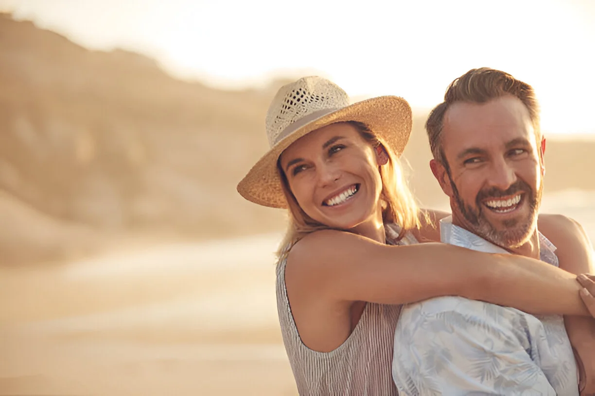 A happy couple laughing and embracing on a Del Mar beach at sunset, representing a renewed sense of health and well-being after successful stem cell therapy.