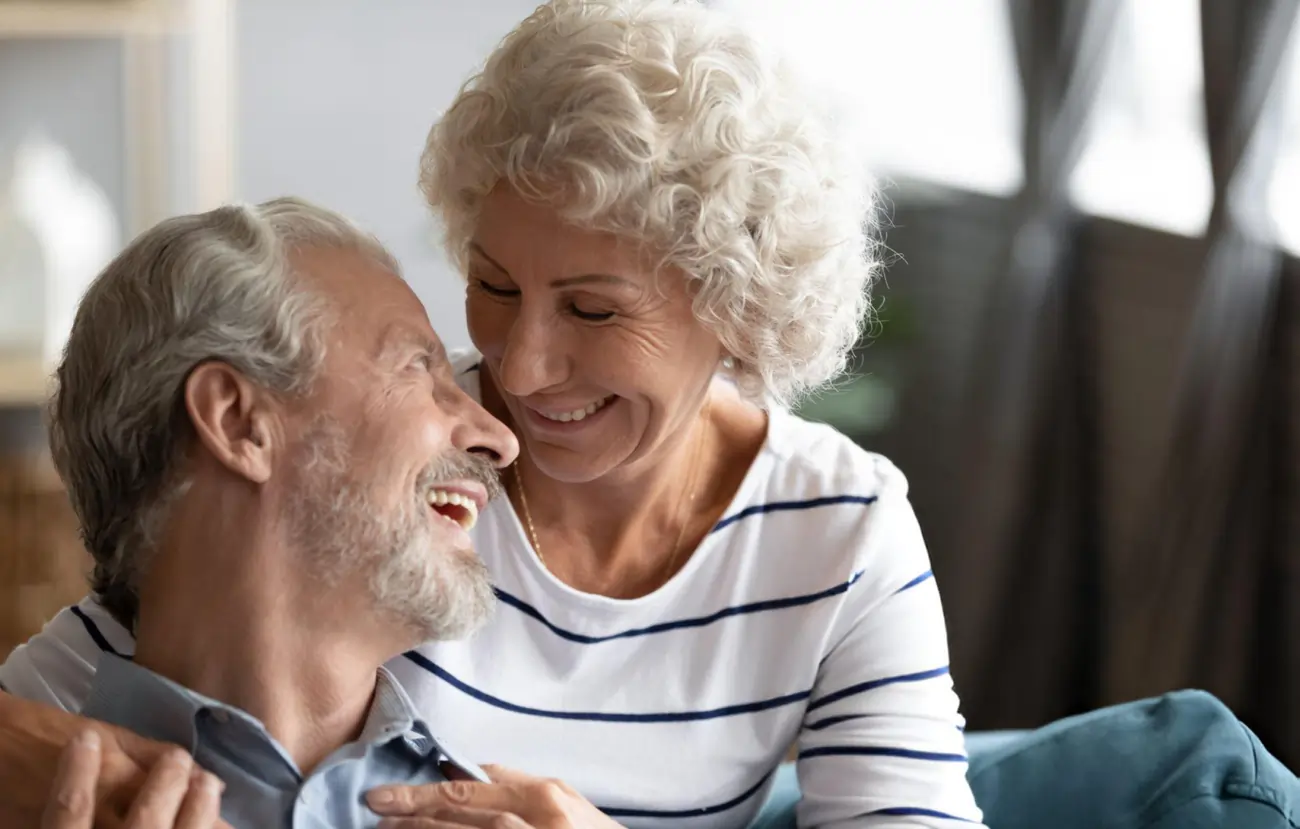 A happy and healthy-looking senior couple embracing and smiling on a couch, representing the improved quality of life and well-being after stem cell therapy in Fair Lawn, New Jersey.