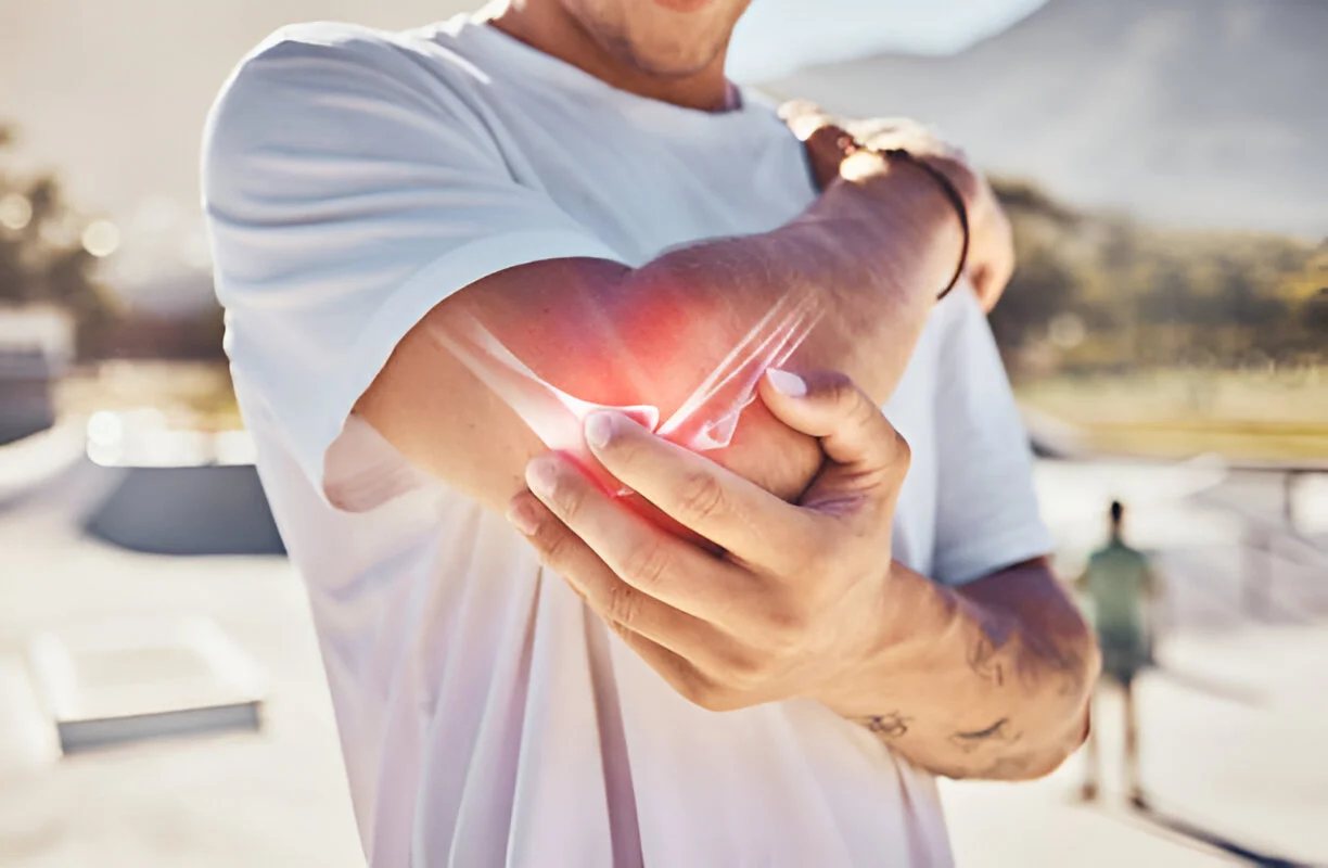 A man holding his painful elbow with a glowing x-ray overlay, representing an elbow or joint injury treated by advanced stem cell therapy in Liberty Lake, WA.