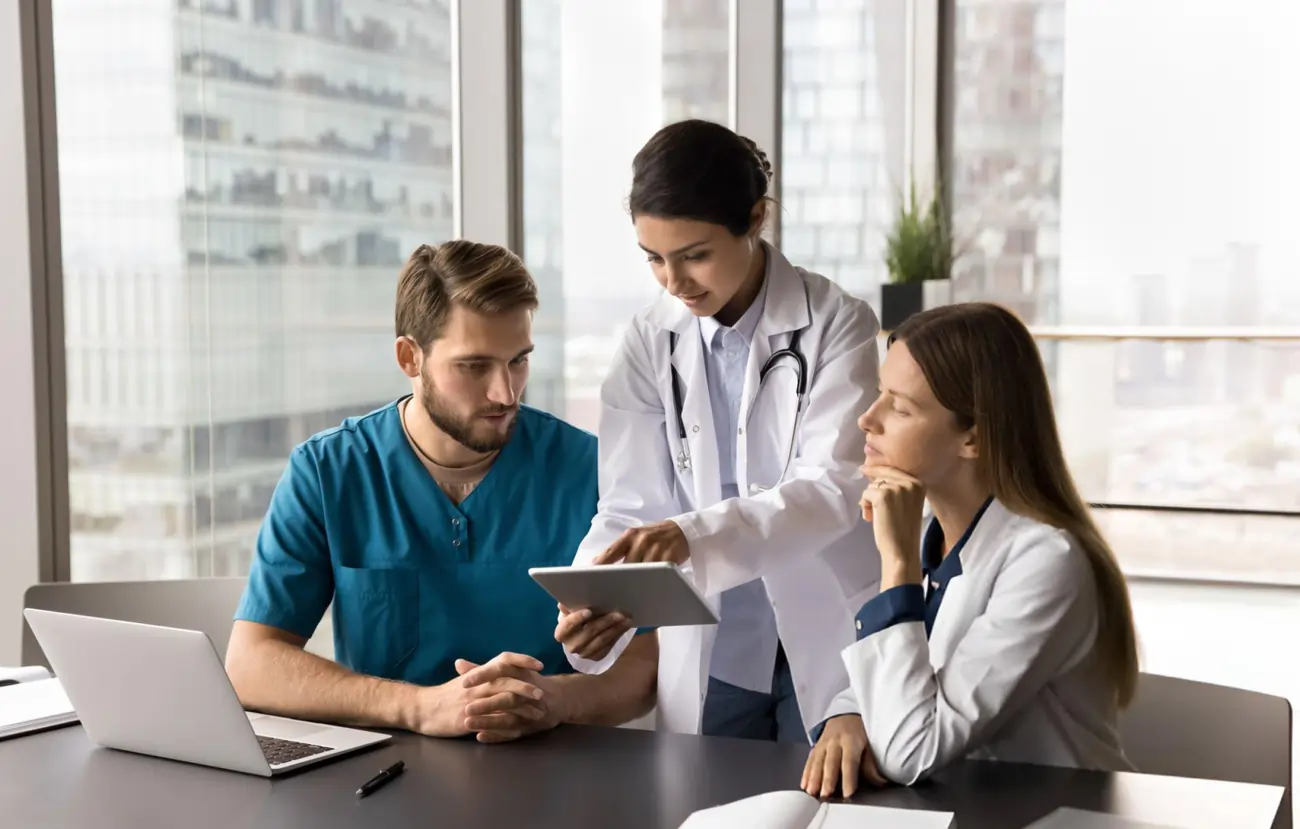A diverse medical team, including a doctor, a surgeon, and a nurse, collaborates while reviewing patient data on a tablet.
