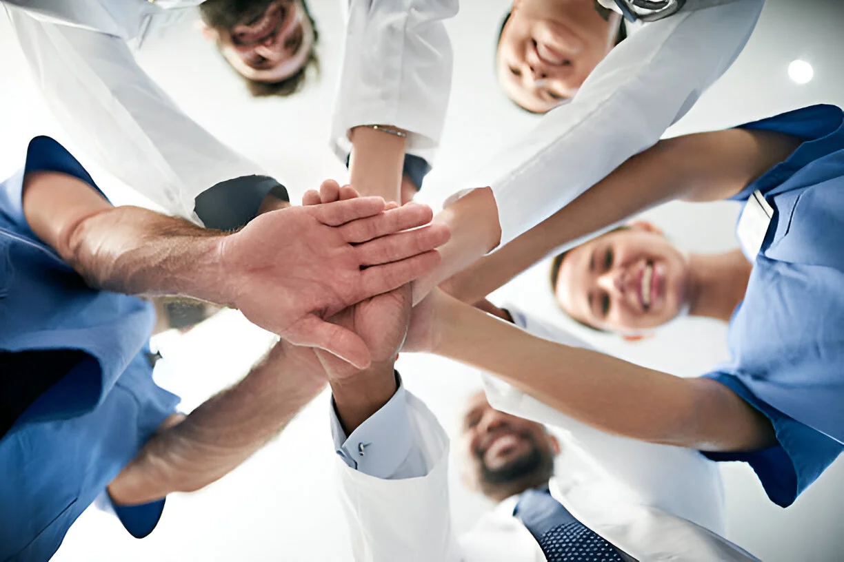A diverse team of medical professionals in a huddle with hands stacked together, representing the collaborative and expert care provided for advanced stem cell therapy in Liberty Lake, WA.