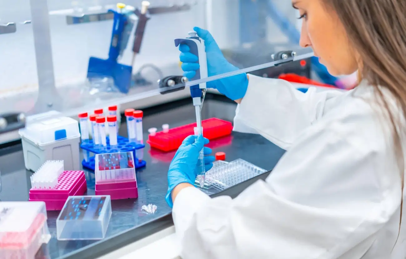 A scientist in a lab coat and blue gloves performs a laboratory procedure with a pipette, representing the advanced research and science behind stem cell therapy.