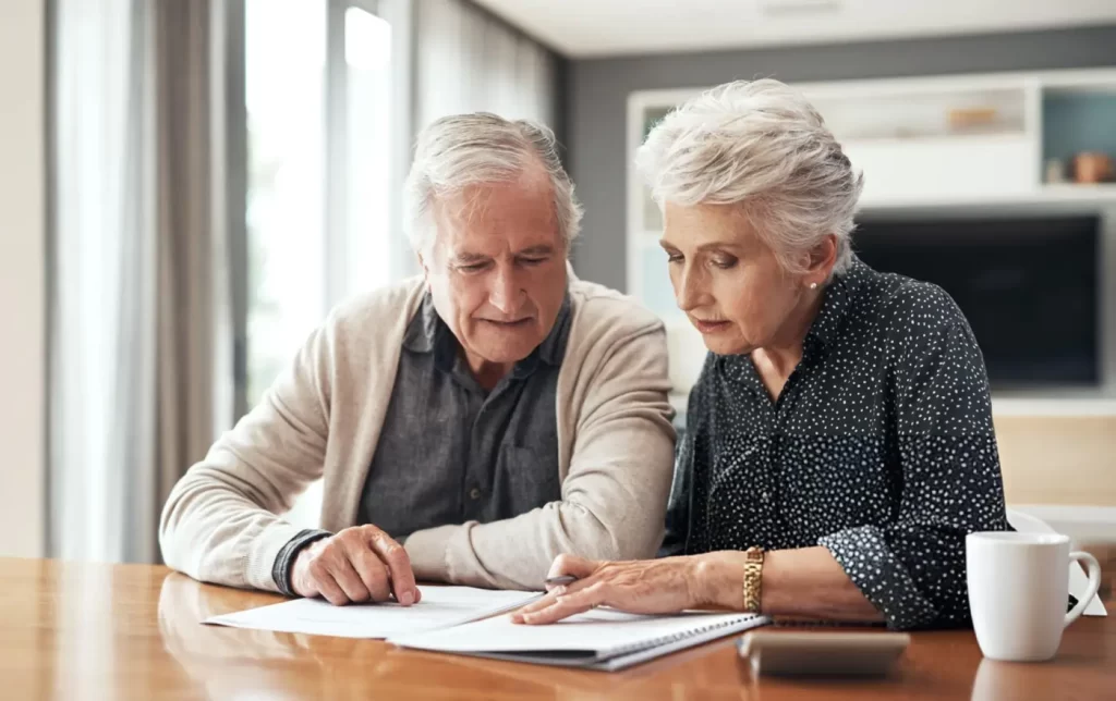 An older man and woman review paperwork together, focused on their finances.