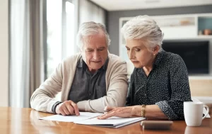 An older man and woman review paperwork together, focused on their finances.