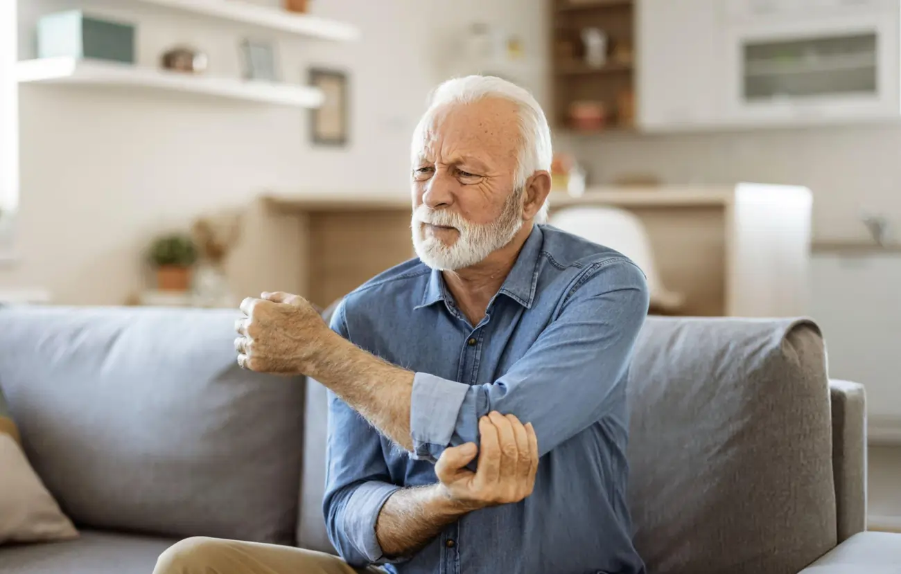 A senior man grimaces in pain, holding his elbow, representing joint pain and chronic conditions that can be treated with stem cell therapy in Jamaica, NY.